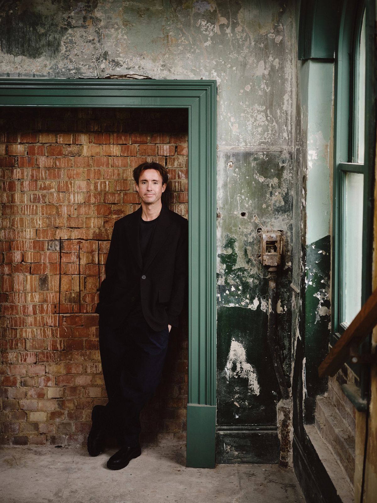 Tom Baddeley standing beside original green joinery and exposed plaster