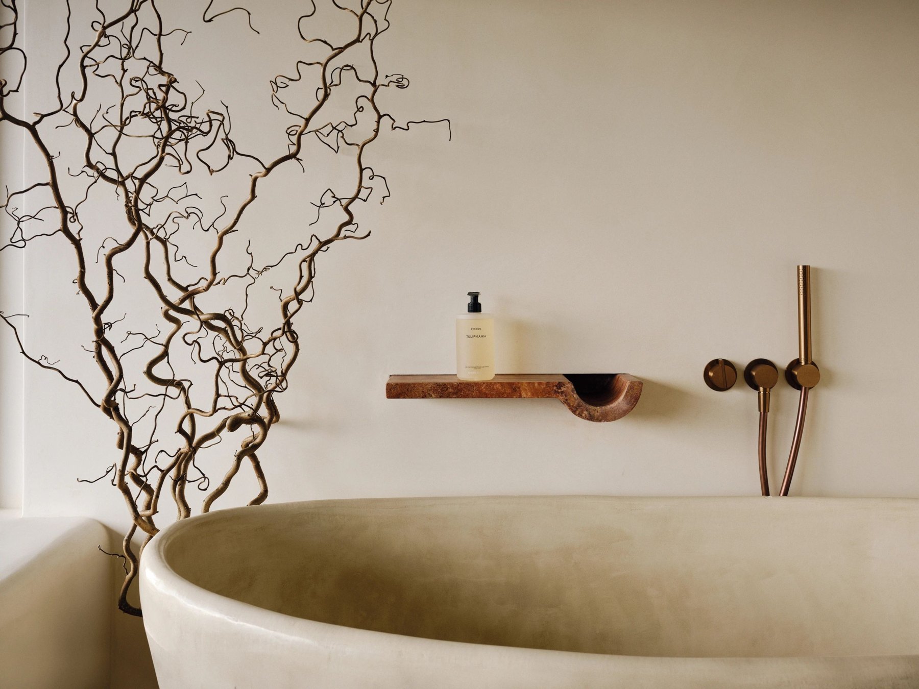 A freestanding stone bath with bronze wall fittings and sculptural branches