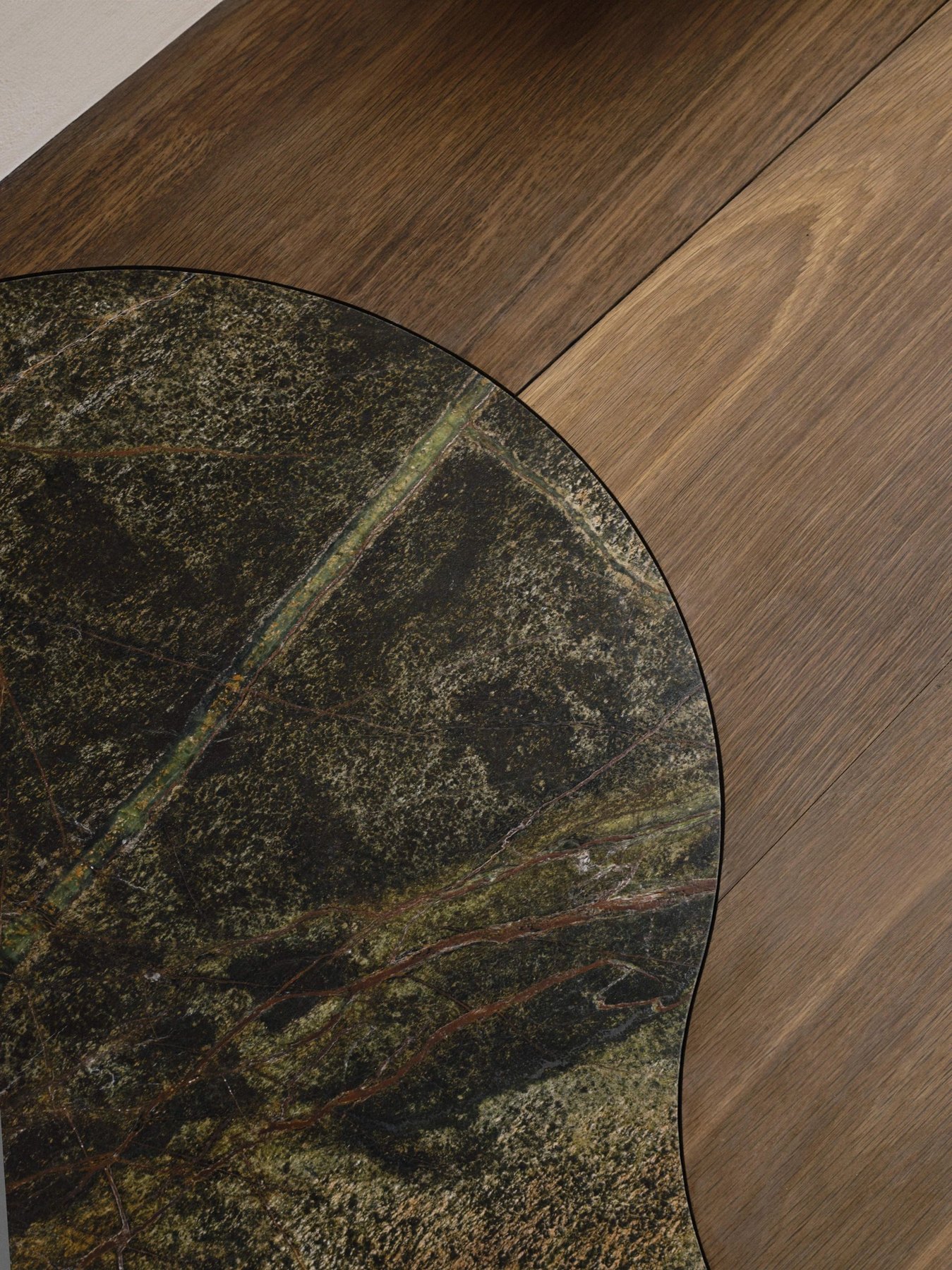 The curved edge of green stone meeting a richly grained timber floor